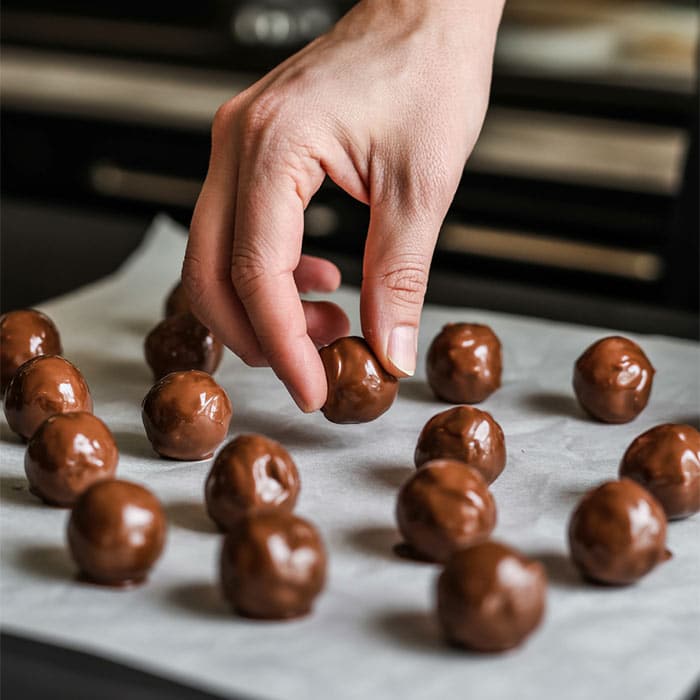 Rolling the chocolate almond butter mixture into bite-sized balls on parchment paper.